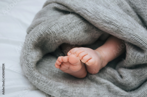 Legs of a young child wrapped in a woolen blanket, close-up on a white bed. The kid sleeps on the sofa, covered with a plaid. Photography, concept.