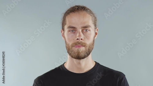 Attractive young serious man look at camera on grey background face t-shirt close up slow motion