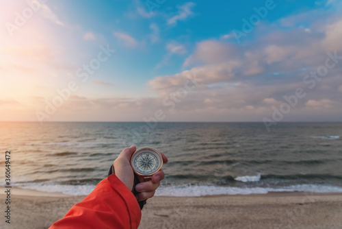 First-person view of a female hand with a compass on a background of a beautiful sea landscape. The concept of navigating the search for your own path and orientation to the cardinal points