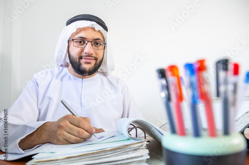 Happy arabic muslim man at work with cup of pens infont of him photo