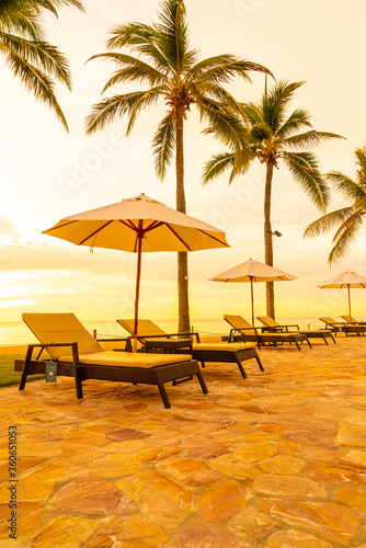 Umbrella and chair around swimming pool in hotel resort with sunrise in morning