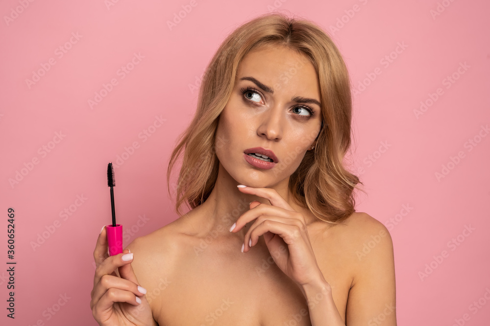 Beauty portrait of a lovely young woman with long blonde hair standing isolated over pink background, showing eye mascara Beauty portrait of a lovely young woman with long blonde hair standing isolated over pink background, showing eye mascara