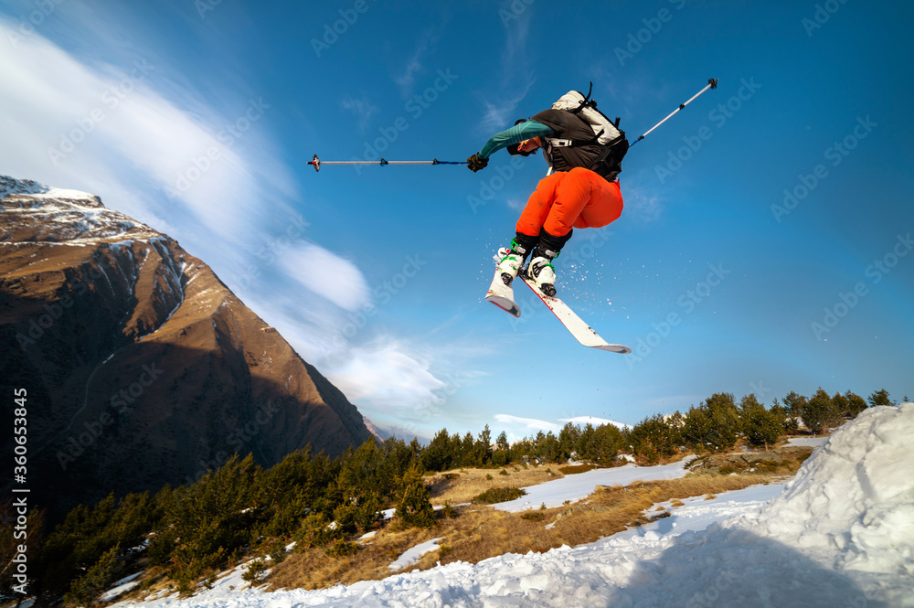 man skier in flight after jumping from a kicker in the spring against the backdrop of mountains and blue sky. Close-up wide angle. The concept of closing the ski season and skiing in spring
