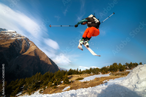 man skier in flight after jumping from a kicker in the spring against the backdrop of mountains and blue sky. Close-up wide angle. The concept of closing the ski season and skiing in spring © yanik88