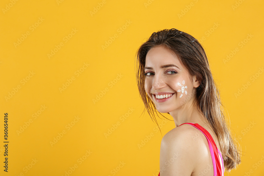 Young woman with sun protection cream on face against yellow background. Space for text Young woman with sun protection cream on face against yellow background. Space for text