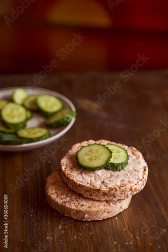 round buckwheat bread on which are two fresh cucumbers on a brown background