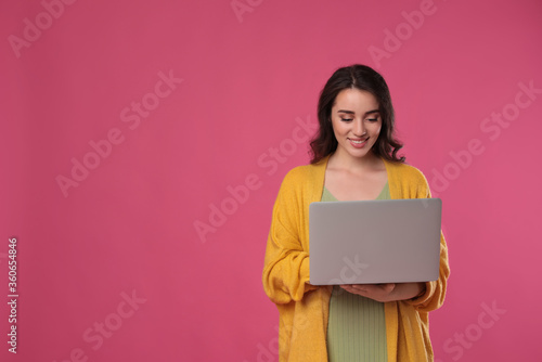 Young woman with laptop on pink background. Space for text © New Africa