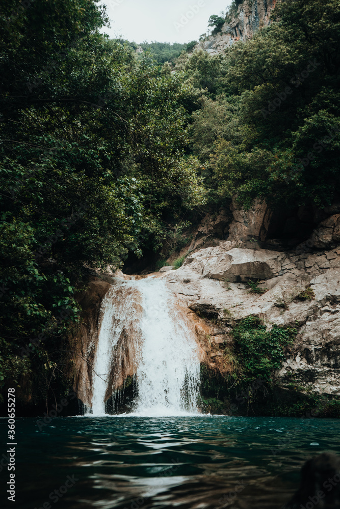 Naklejka premium Vertical photo of a high mountain river waterfall between trees and vegetation