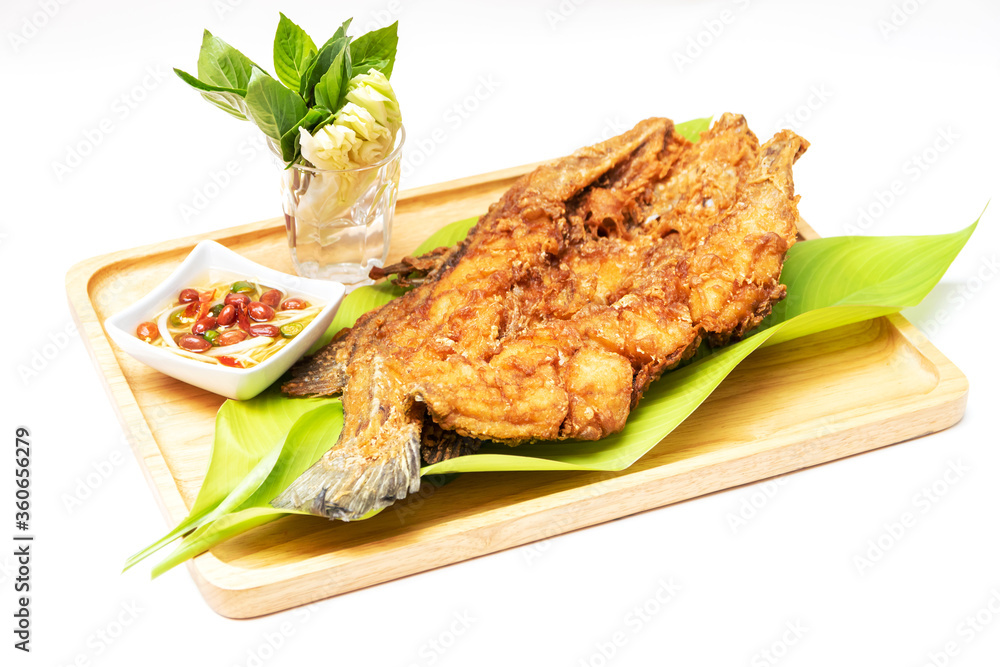 Deep fried sea bass with fish sauce and green mango chili fish sauce, based on chili fish sauce, addition of shredded green mango and lime juice serving on wooden tray isolated on white background.