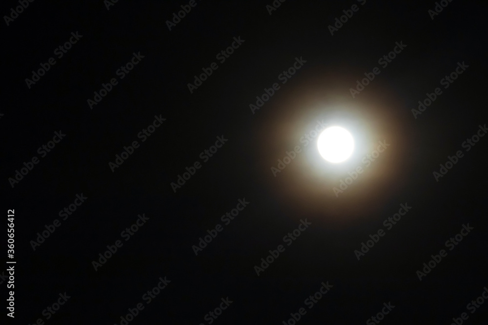 Full moon shining glowing light through the darkness of cloudy night sky; long exposure for beautiful nature background. Full moon shining glowing light through the darkness of cloudy night sky; long exposure for beautiful nature background.