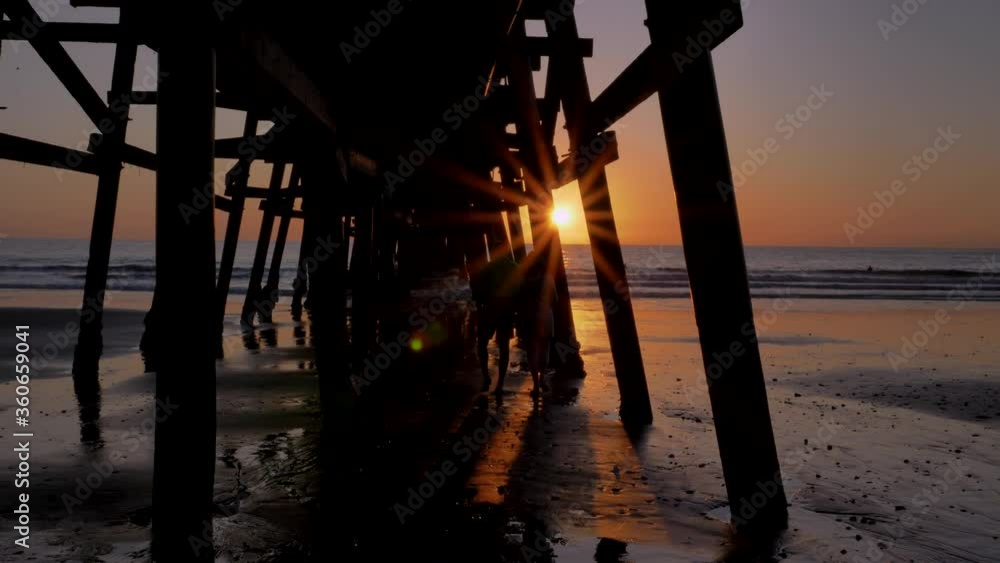 Couple walking wide shot holding hands together at Scenic orange pink Sunset with epic rays of light and sun flare wooden pier in San Clementa California Couple walking wide shot holding hands together at Scenic orange pink Sunset with epic rays of light and sun flare wooden pier in San Clementa California