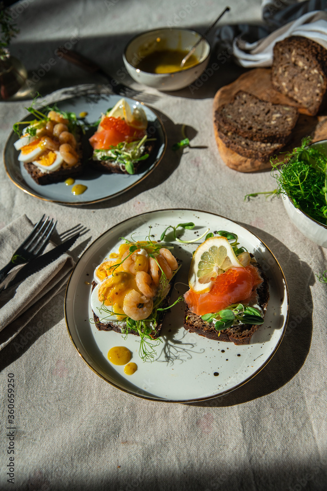 Smorrebrod dinner. Traditional Danish homemade  open rye bread sandwiches with smoked salmon and caviar and shrimps and egg both with microgreens served on ceramic plates on linen tablecloth.