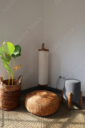 Aesthetic interior. Sitting corner has floor lamp, floor mat, plants and chair. Plants basket and chair made from water hyacinth. Sun shines through window
