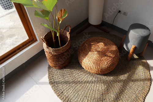 Aesthetic interior. Sitting corner has floor lamp, floor mat, plants and chair. Plants basket and chair made from water hyacinth. Sun shines through window