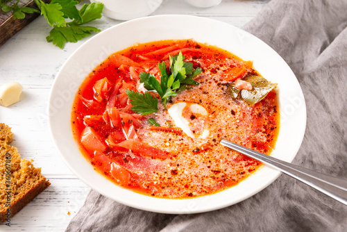 Russian traditional vegetable soup, borscht with sour cream and parsley in a white plate, spoon, on a gray napkin on a white background