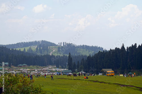 many people enjoying and relaxing holidays in the hills covered with green forests and green meadows.