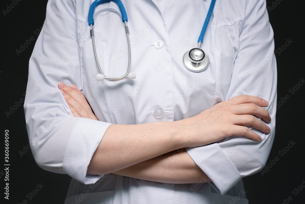 Woman a doctor is standing with crossed arms close up on dark background. Woman a doctor is standing with crossed arms close up on dark background.