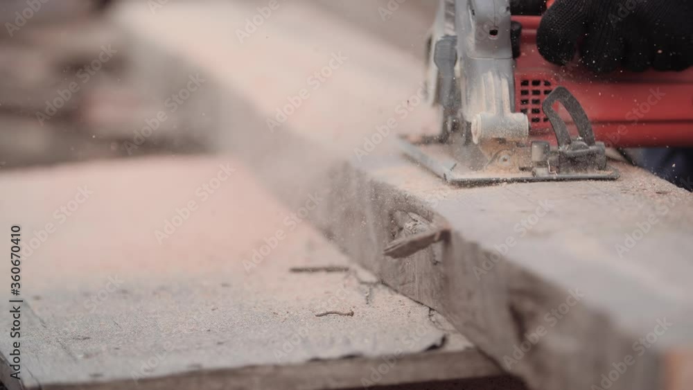 Close-up of flying sawdust from working electric circular saw on tree in hands of unidentified man in slow motion. Worker cuts board with modern grinder. Repair concept of frame housing construction. Close-up of flying sawdust from working electric circular saw on tree in hands of unidentified man in slow motion. Worker cuts board with modern grinder. Repair concept of frame housing construction.