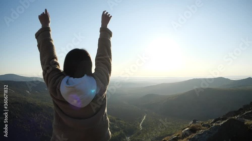 A girl enjoys the dawn in the mountains. The woman is stretching just up the mountain. She enjoys watching beautiful landscape.Young woman on top of the mountain
