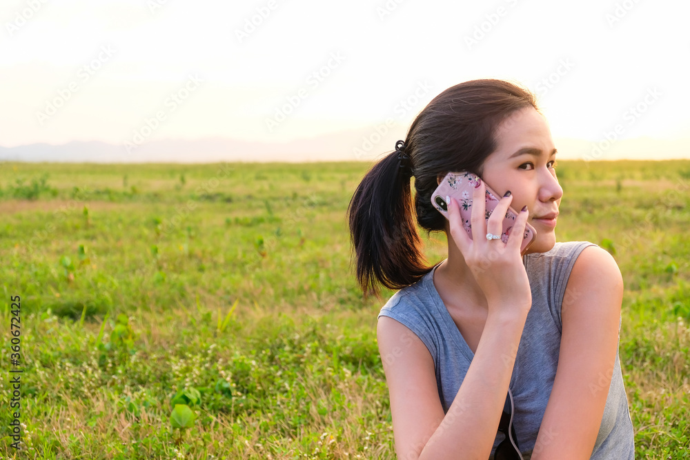 Selective focus of Asian women taking on mobile phone with green grass and sunset nature background Selective focus of Asian women taking on mobile phone with green grass and sunset nature background