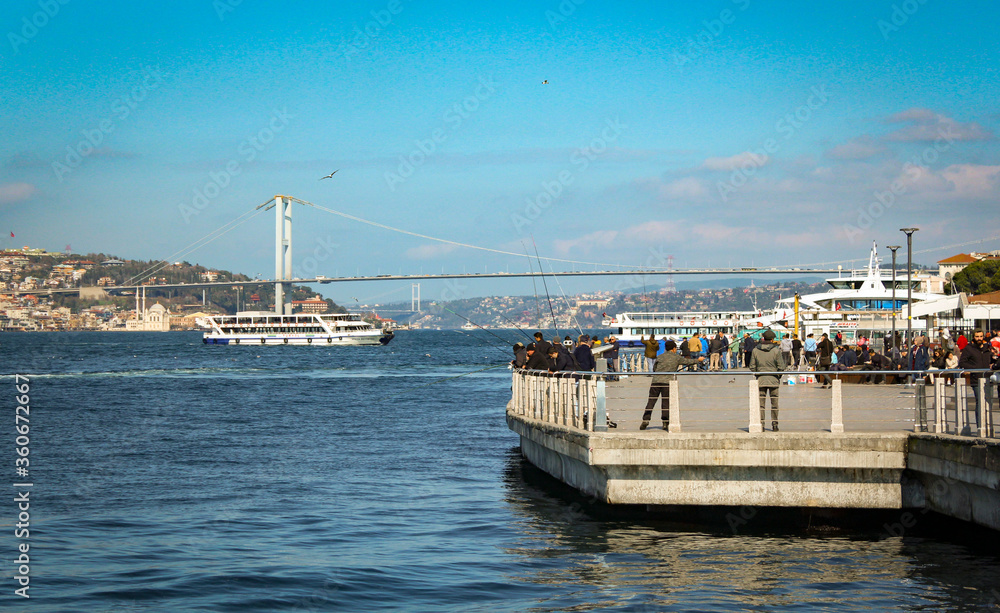 People are fishing in Uskudar, a district in Istanbul near the port. Two bridges, Ortakoy mosque are also visible in the background. Fantastic view. Seagulls on air.