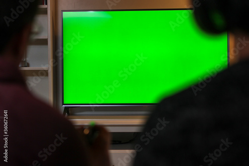 Woman and man are sitting next to each other at home looking at Green Chroma Key Screen, Relaxing on a Couch. Husband holds remote controller in his hand. Couple is watching TV Concept.