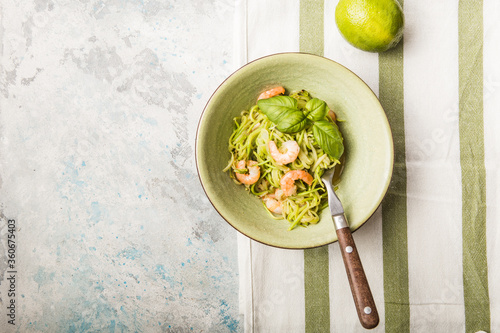 Zucchini Vegetable noodles - green zoodles or courgette spaghetti  with shrimps on plate over gray background. Clean eating, raw vegetarian food concept. Copy space for text. Top view or flat lay photo