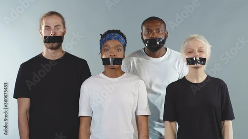 Group of people with tape on mouth look at camera grey background silence gender freedom equality discrimination movement crisis citizen censorship international slow motion photo