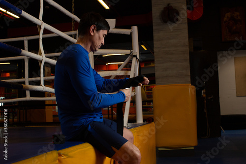 Hands of boxer against a background fitness room. Sporty man during boxing. boxer rewinds his hands with black elastic bandage preparing to workout in dark boxing studio