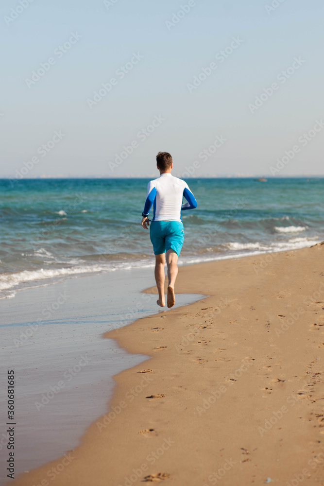 A male athlete runs along the beach in blue shorts along the sea. Coast of Cyprus. Copy space.