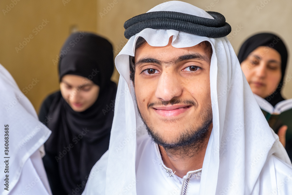 Muslim guy wearing arabic clothes sitting with his family reading quran together Muslim guy wearing arabic clothes sitting with his family reading quran together