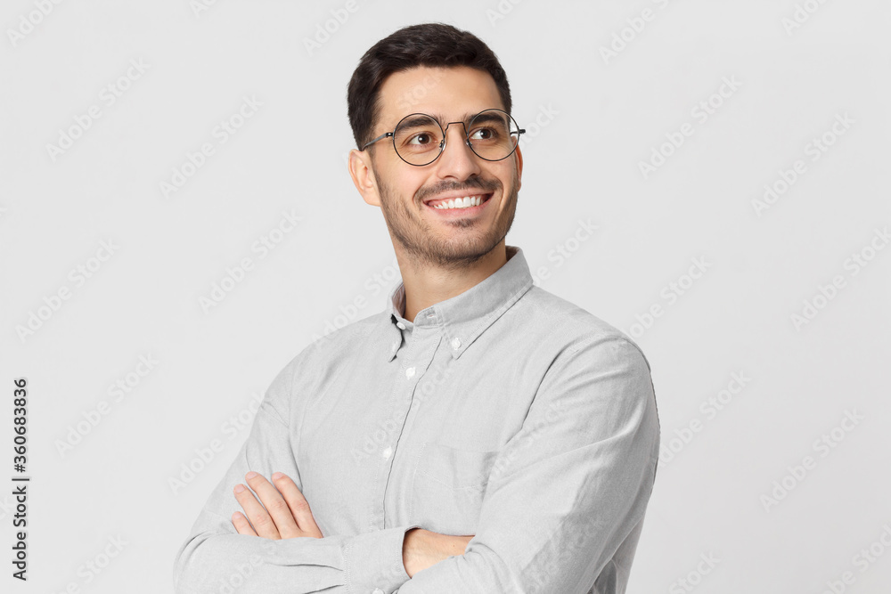 Portrait of young handsome smiling man dressed in shirt and eyeglasses, standing with arms crossed, looking away, isolated on gray background - obrazy, fototapety, plakaty 