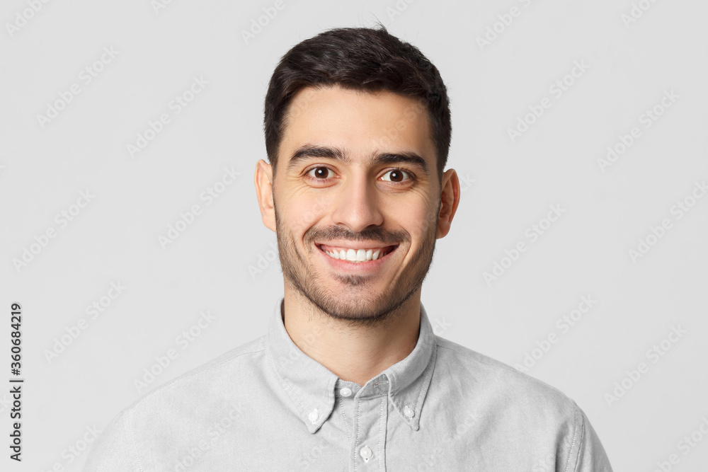 Close up portrait of young smiling handsome man wearing gray shirt, feeling confident as professional, isolated on studio background Close up portrait of young smiling handsome man wearing gray shirt, feeling confident as professional, isolated on studio background