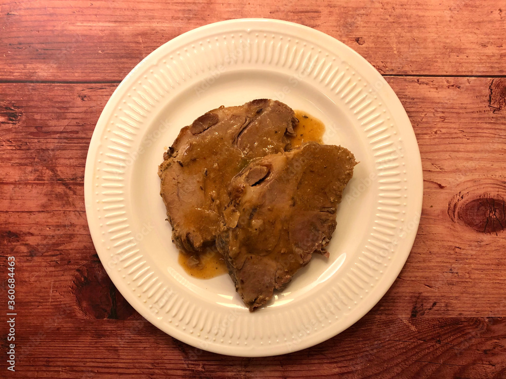 Roast pork with gravy on white plate. 