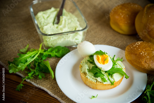 Homemade bun with cheese spread, fresh arugula and boiled egg in a plate