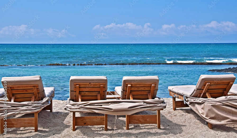 These lounge chairs are just waiting for someone to slip into to sun bathe in, on this beautiful tropical beach.  Turquoise colored ocean water and white sands of Hawaii.