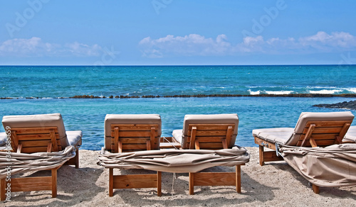 These lounge chairs are just waiting for someone to slip into to sun bathe in  on this beautiful tropical beach.  Turquoise colored ocean water and white sands of Hawaii.