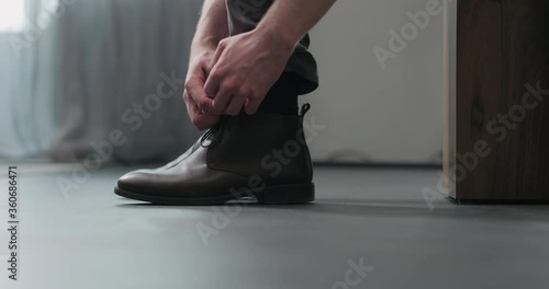 Slow motion man unlace his brown leather chukka boots indoor photo