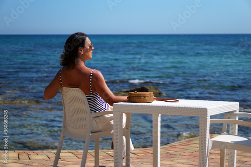 A woman is sitting in an outdoor cafe near the sea