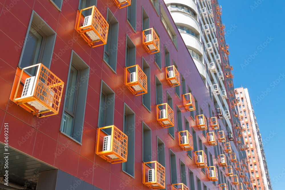 Corporate orange building facade wall with many air-conditioners on blue sky background