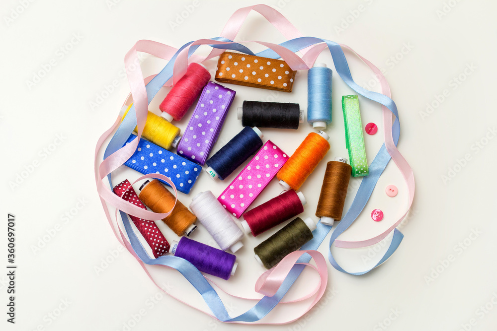 Fototapeta premium Sewing kit. Composition with threads and sewing accessories on a white background, an even layer. Colored satin ribbons