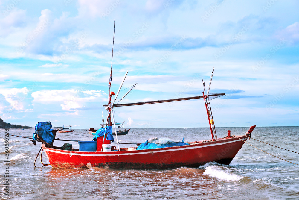 Sideview old small red fishing boat float on the sea with beautiful blue sky background.