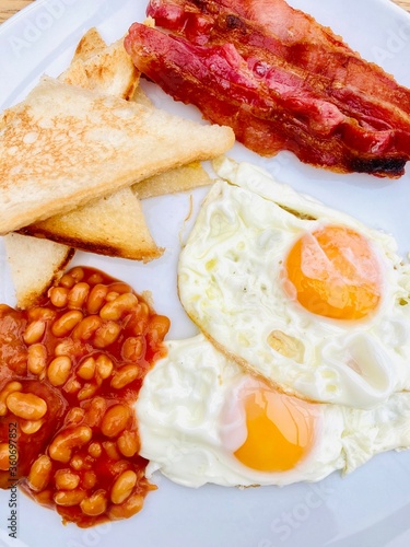 English cooked breakfast with fried eggs, fried bread, baked beans and crispy bacon