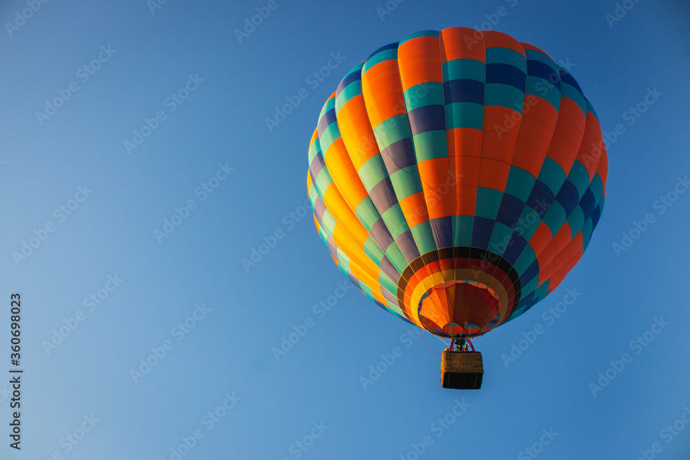 Naklejka premium Hot air balloon in clear blue sky. Colorful balloon with basket lift up. Aircraft concept. Summer adventure and leisure. Aviation sport concept. Bright orange balloon in calm morning. Flight concept.