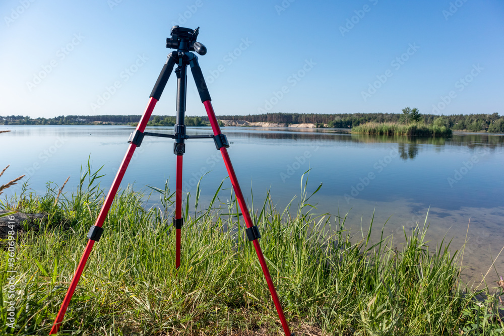 custom made wallpaper toronto digitalCamera red tripod standing in green grass near lake water natural landscape on clear sunny bright day