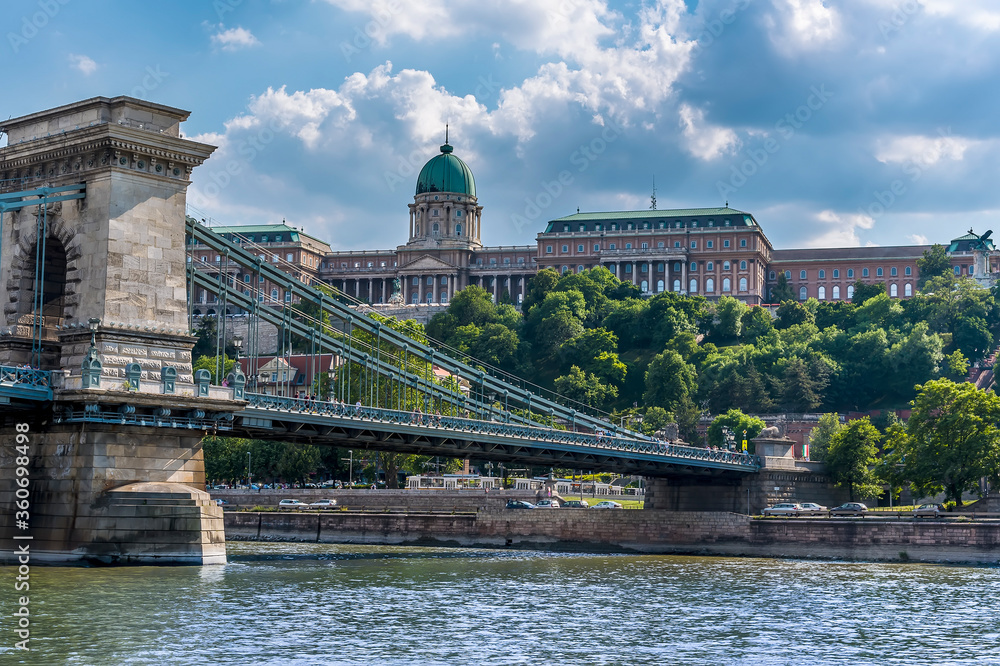 The Chain Bridge reaches the western shore of the River Danube below the Royal Palace in Budapest in the summertime