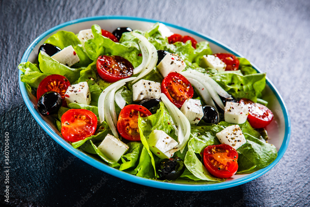 Fresh Greek salad - feta cheese, cherry tomatoes, lettuce, black olives and onion on black stone board
