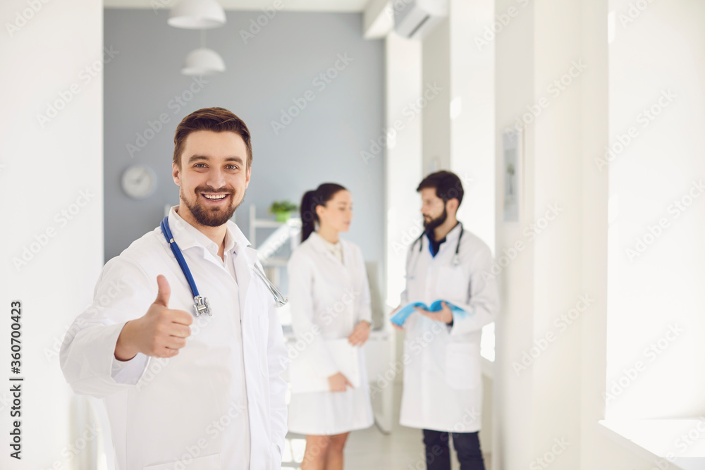 A practicing doctor with a stethoscope smiles against the background of a doctor at the clinic.