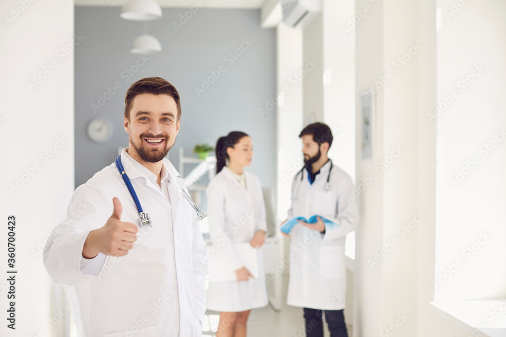 A practicing doctor with a stethoscope smiles against the background of a doctor at the clinic. A practicing doctor with a stethoscope smiles against the background of a doctor at the clinic.
