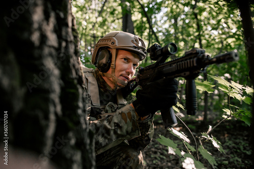 Army soldier in camouflage sitting in an ambush in the forest often hiding behind a tree